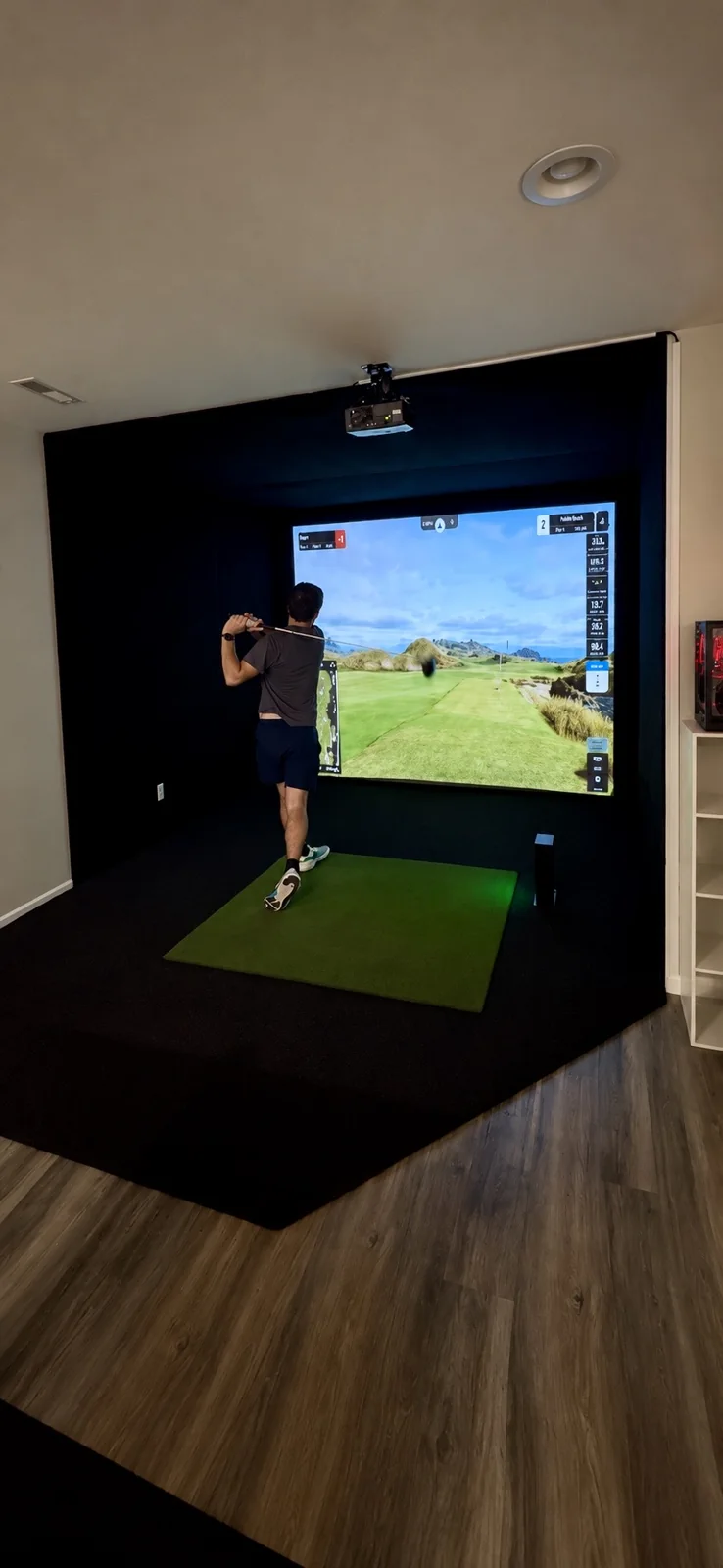 Completed SIMHAUS basement golf simulator with black enclosure, projected golf course and golfer swinging