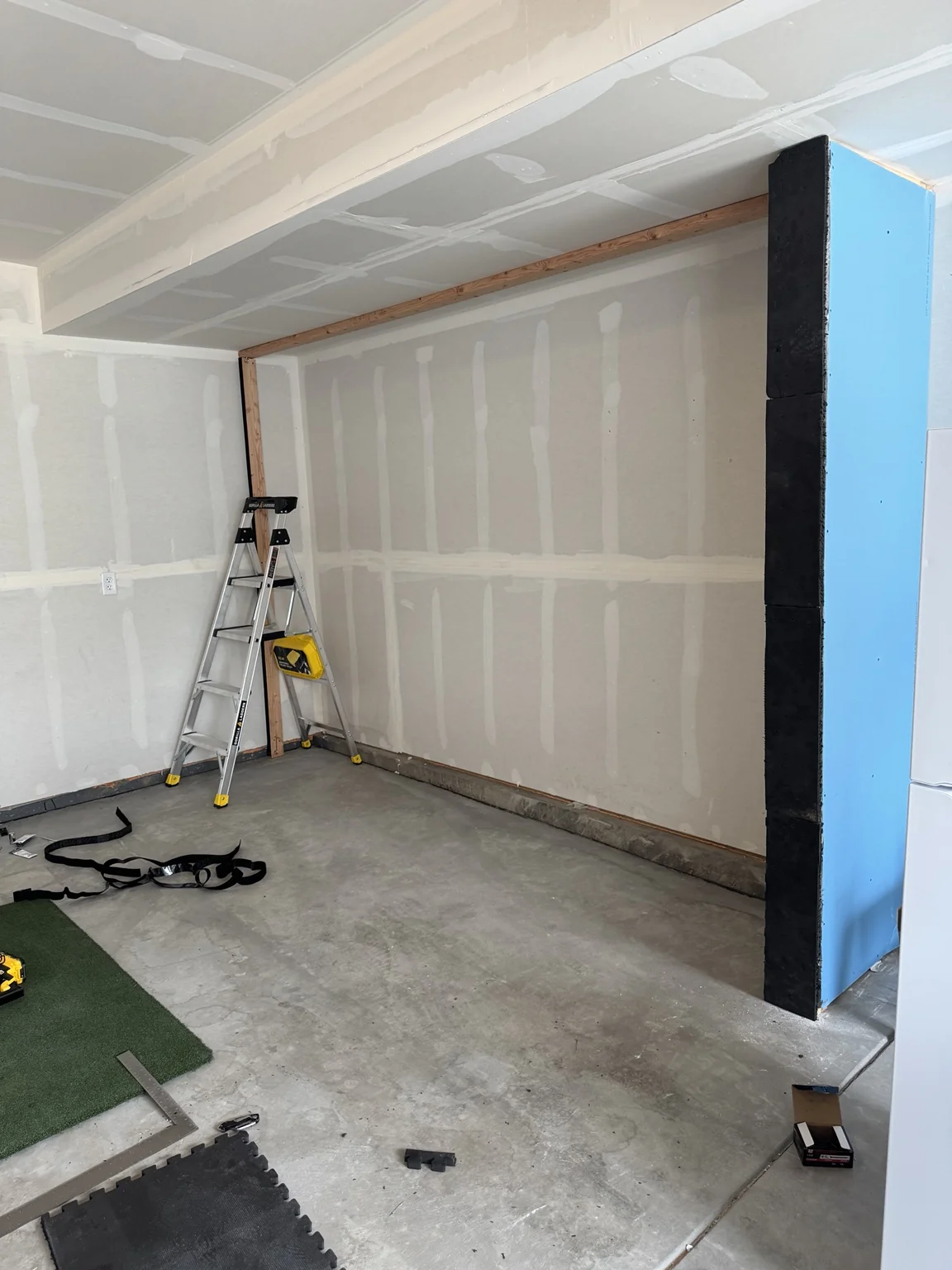 Garage during golf simulator installation, showing unfinished drywall and bare concrete floor