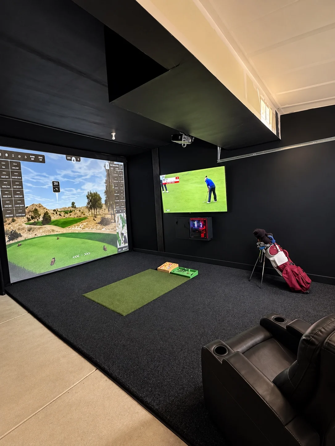 Completed SIMHAUS garage golf simulator with black walls, impact screen, TV and lounge seating