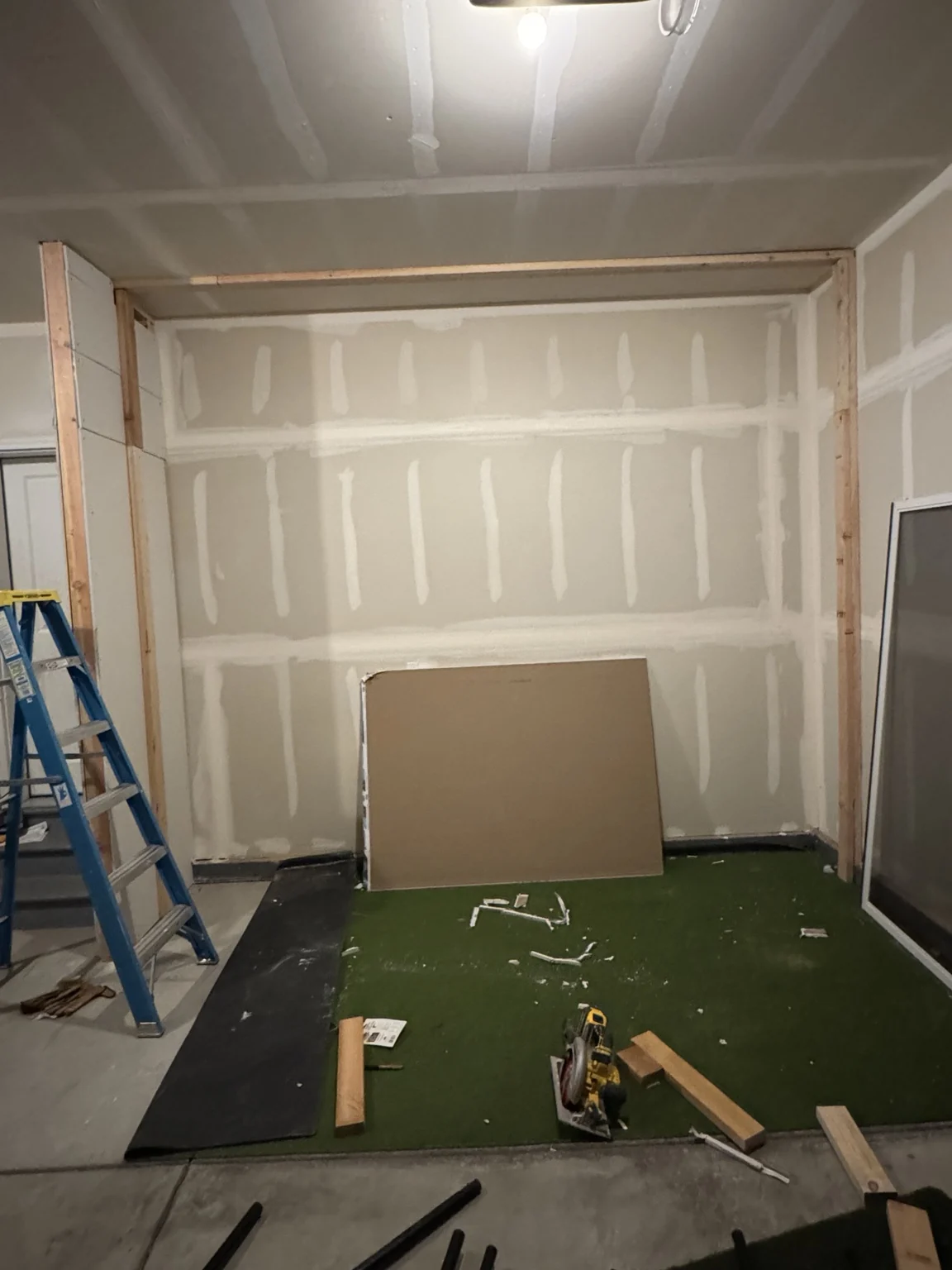 Garage golf simulator construction in progress with exposed framing and hitting turf